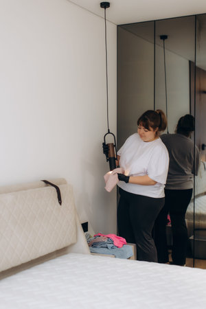 Woman in gloves cleaning a hanging lamp with a cloth, providing housekeeping services in a tidy bedroomの写真素材