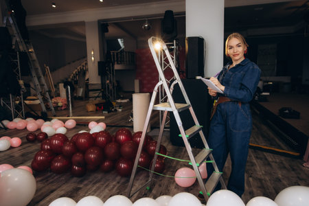 Professional event planner woman making notes, organizing a party preparation in a spacious room with many balloonsの写真素材