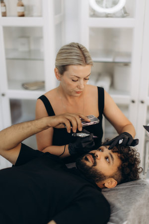 Professional beautician applying permanent makeup on client's eyebrows in a beauty professional...