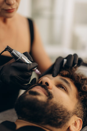 Man getting permanent makeup applied to his eyebrows by a technician. Beauty procedure for cosmetic...