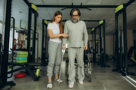 Physiotherapist helping an elderly man with a crutch walk in a gym for physical therapy and recovery
