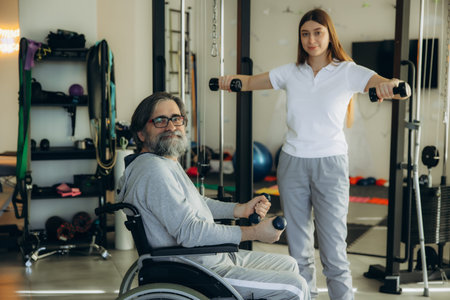 Physiotherapist assisting disabled man in wheelchair performing rehabilitation exercises with...