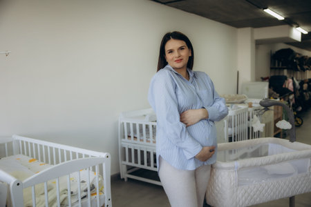 Pregnant woman posing with hands on belly, smiling while shopping for a baby crib for her future...