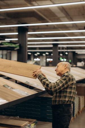 Senior man carefully selecting planks of wood laminate flooring for home renovation in a modern...
