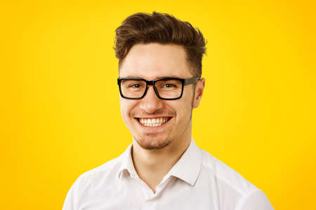 Funny young man wearing white shirt and glasses posing on yelllow background の写真素材