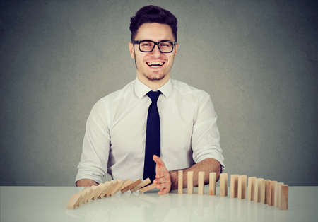 Businessman stopping the domino effect. Concept for business solution, strategy and successful interventionの写真素材