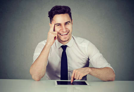 Successful young business man with tablet sitting at desk smiling looking at camera の写真素材