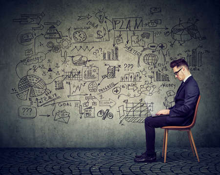 Businessman working with laptop on a business plan on the wall background full of economy drawingsの写真素材