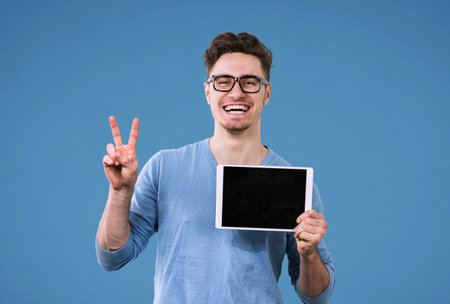 Happy hipster man in glasses with tablet computer giving victory sign 
