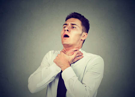 Young man having asthma attack or choking can't breath suffering from respiration problems isolated on gray background  の写真素材