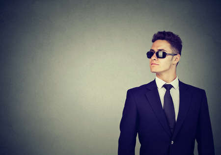 Business guy in sunglasses and suit on gray wall background, looking awayの写真素材