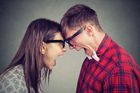 Side view of man and woman in glasses yelling at each other standing head to head in quarrel. の写真素材