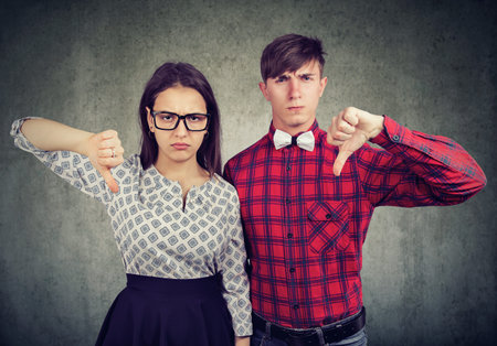 Unhappy grumpy couple giving thumbs down gesture, disagree with something. Displeased young man and...