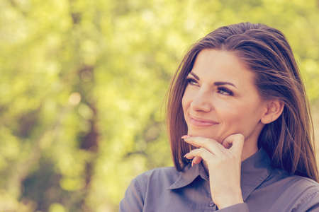 Portrait of a happy woman in park on sunny autumn afternoon. Cheerful beautiful girl in gray shirt and outdoors on beautiful fall day. Back lit, natural light.の写真素材