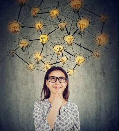 Cute woman in glasses with many ideas light bulbs above head looking up isolated on wall background.の写真素材