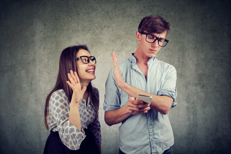 Annoying woman trying to distract young handsome man ignoring her while using a smartphone browsing...