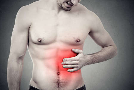 Muscular man with stomach pain on gray backgroundの写真素材