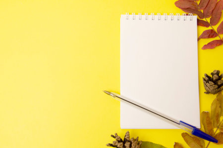 Blank open notepad with pen and autumn leaves on yellow background. Mockup Copy space Top view Flat...