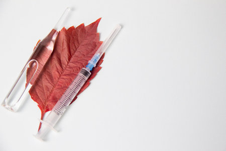 Syringe and ampoule with medicine lying on red wood sheet on white backgroundの写真素材