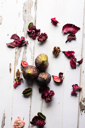 Fresh figs and dried rose petals on white wooden background.