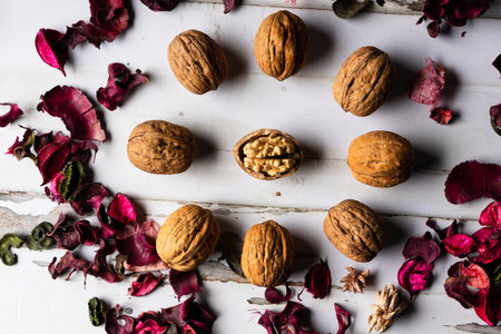 Walnuts and dried rose petals on a white wooden background.の写真素材