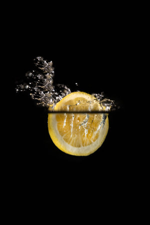 slice of lemon falling into water with bubbles isolated on black background.の写真素材