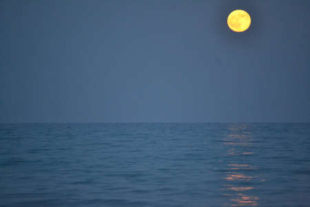 The moon rising over the horizon of the Mediterranean Sea. Photo taken from the shore of Benicasim beach, in CastellÃ³nの写真素材