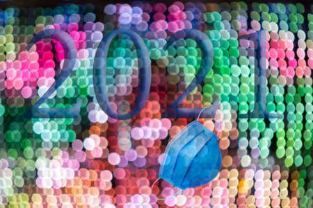 Text with the number of the year 2021 with a background of bright out of focus lights in various shades with Bokeh effect and a disposable hygienic mask. Happy New Year 2021.の写真素材