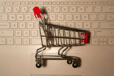 Realistic iron mini shopping cart with red plastic parts on top of a computer keyboard. Object for purchases such as sales, Black Friday or Christmas shopping. White background. Horizontal photographyの写真素材