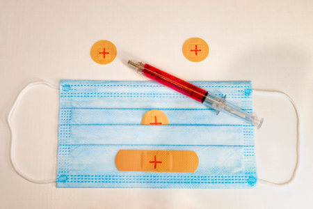 Blue disposable surgical mask with rectangular and circular band-aids forming a face and a red...