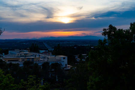 Sunset. Sunset with high clouds leaving the sky orange and blue. Backlight of the leaves and branches of the trees in a park in Madrid, in Spain. Europe. Horizontal photography.の写真素材