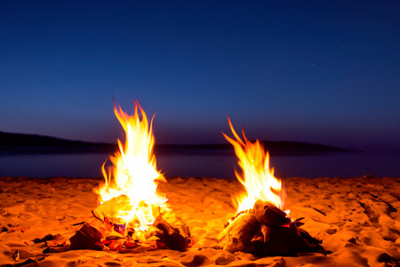 Bonfire. Small campfire with gentle flames beside a lake during a glowing sunset. San Juan night on the beach. People jumping over the bonfires. Bonfire at night.の素材