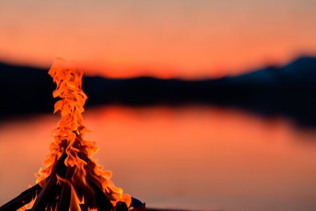 Bonfire. Small campfire with gentle flames beside a lake during a glowing sunset. San Juan night on the beach. People jumping over the bonfires. Bonfire at night.の素材