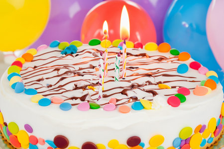 Birthday cake. Celebration birthday cake with lots of icing and decorations. Image for postcard. Celebration concept. Beautiful birthday cake with burning candles on stand againstの写真素材