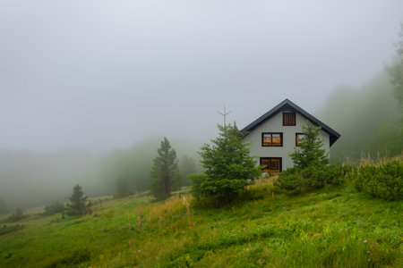 Isolated house in the mountains, beautiful typical northern European house in a lush, green landscape with fog. Beautiful summer landscape with green meadows and house in the mountの写真素材