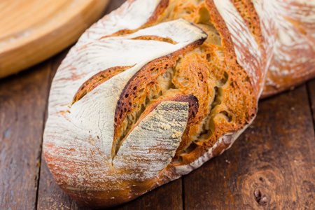 Bread. Close up of rustic bread loaf on wooden table. Baker or chef holding fresh made bread....