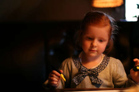 Little cute redhead girl painting on the table with yellow pen on the darkの写真素材
