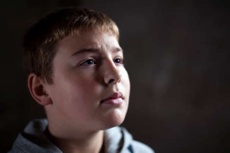 Young boy looking up with hope in his eyes against grunge background flash lit 3 light sourcesの写真素材