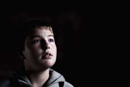 Young boy looking up with hope in his eyes against grunge background flash lit 3 light sourcesの写真素材