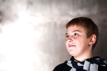 Young boy looking up with hope in his eyes against grunge background flash lit 3 light sourcesの写真素材