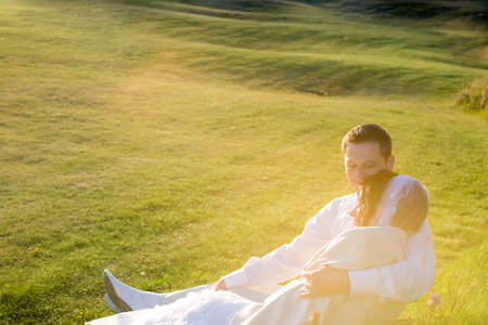 Bride and groom on the grass looking at sunset and last rays of evening sunの写真素材