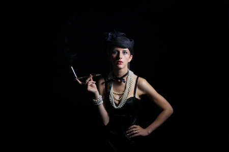 Woman with cigarette and vintage hat with long legs against dar backgroundの写真素材