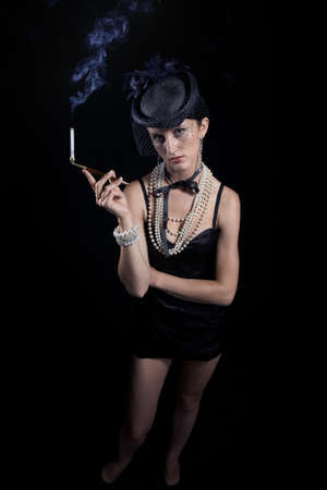 Woman with cigarette and vintage hat with long legs against dar backgroundの写真素材