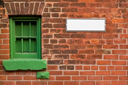 Red brick wall with green window and blank signの写真素材