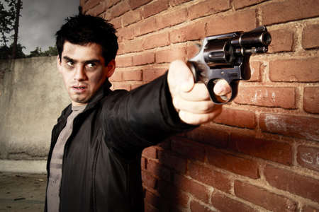 man with gun besides a brick wallの写真素材