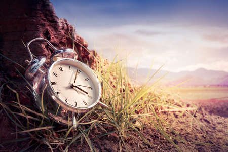 alarm clock sitting on the grass at sunset or sunriseの写真素材