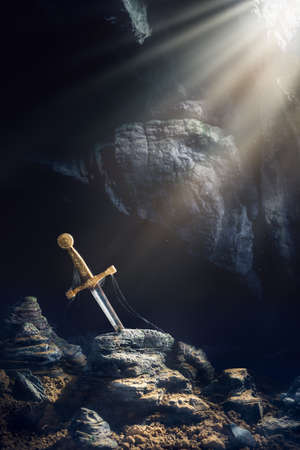High contrast image of Excalibur, sword in the stone with light rays and dust specs in a dark caveの写真素材