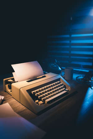 High contrast image of a retro typewriter with a blank sheet of paper on a wooden backgroundの写真素材