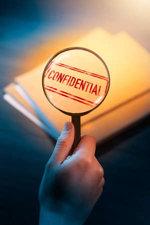 Private investigator holding a magnifying glass focusing on confidential envelopesの写真素材