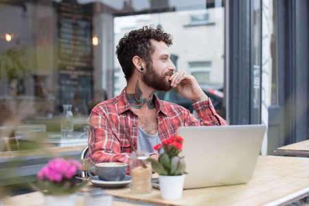Young tattooed hipster using his laptop, sat outside a cafeの写真素材